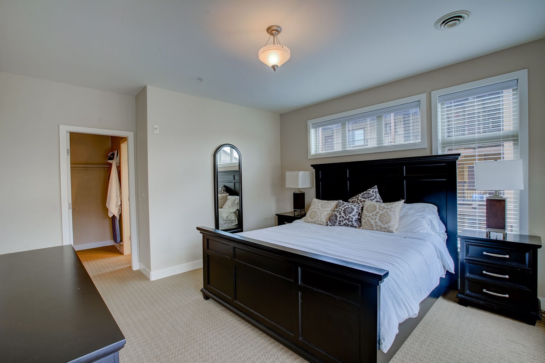A bedroom with a dark wood bed, a nightstand, a mirror, and a window with blinds.