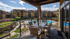 Un balcon doté d’une table en verre et de chaises en osier, offrant une vue sur une piscine et sur des immeubles résidentiels à plusieurs étages.