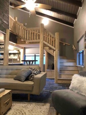 A cozy interior with a wooden staircase, a sofa, and a fluffy white chair.