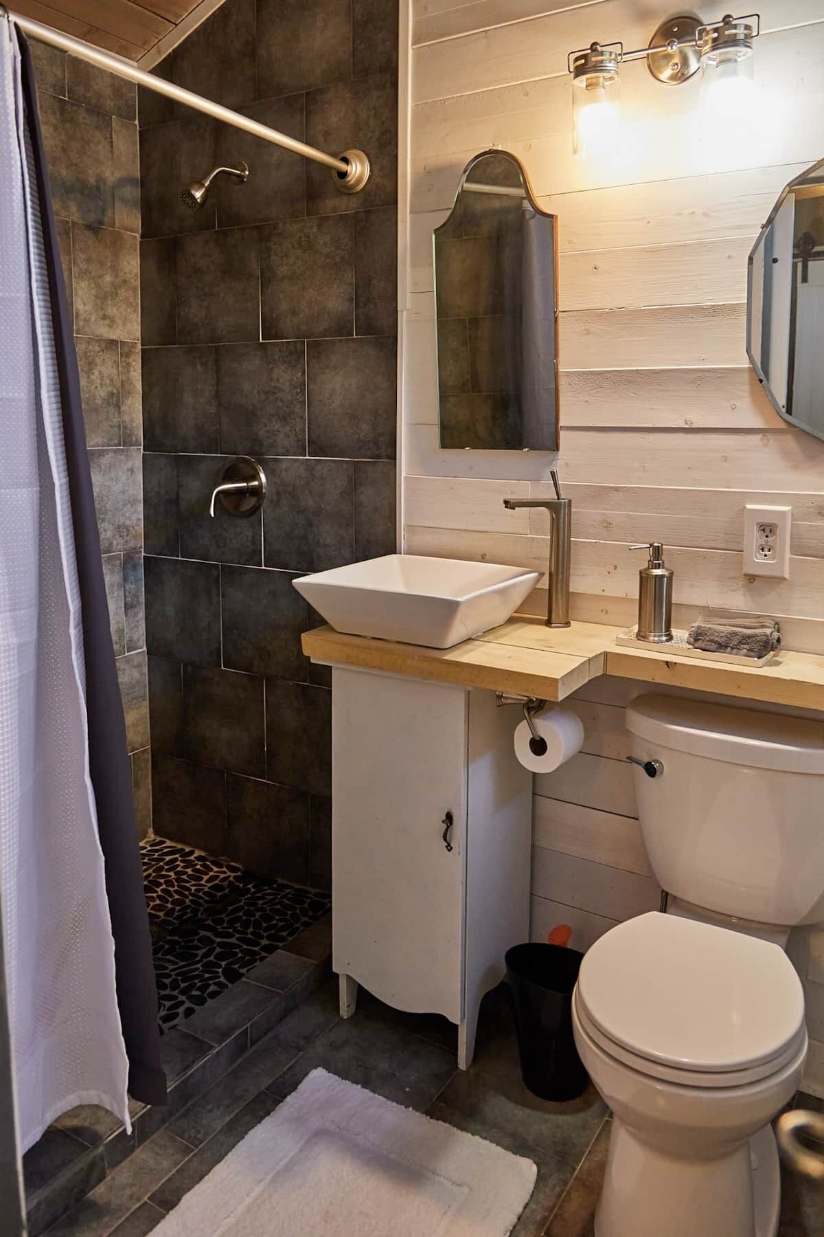 Un baño con ducha, lavamanos, inodoro y espejo.