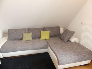 A grey sectional sofa with two yellow cushions, white cushions, and a white armchair in a room with a black carpet and white walls. - Anneliese by Interhome (Saalfelden am Steinernen Meer)