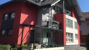 A two-story house with a red facade, a balcony with a railing, and a glass entrance. - Anneliese by Interhome (Saalfelden am Steinernen Meer)