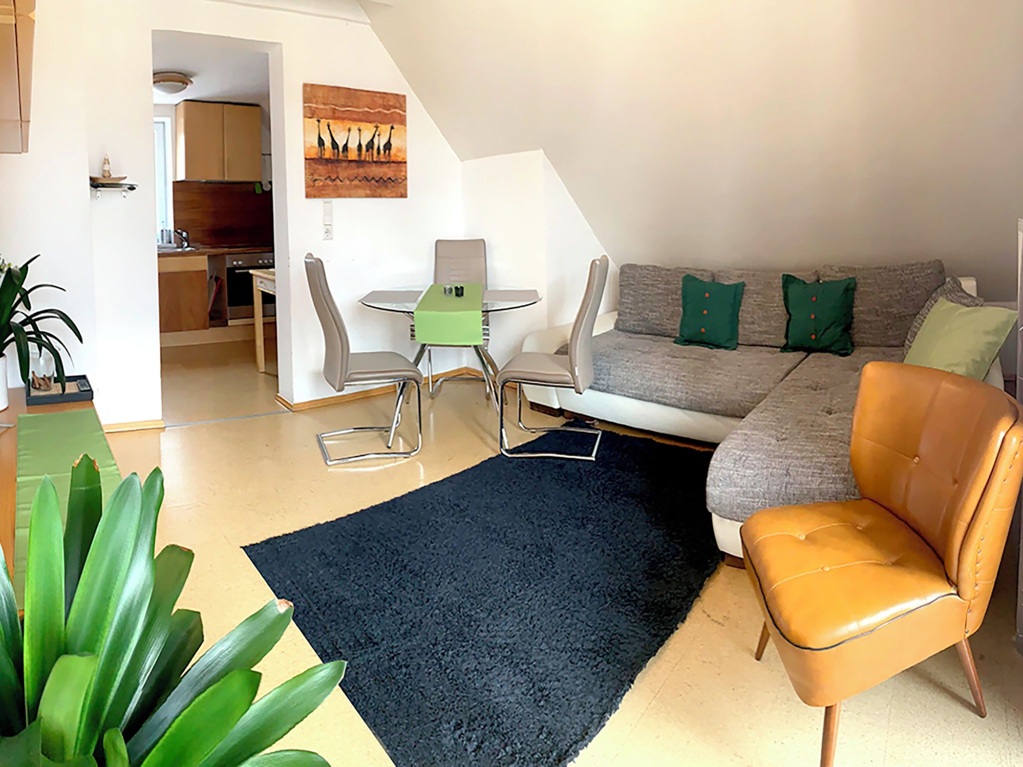 Una sala moderna con un sofá, una mesa de comedor con sillas, un tapete negro y una planta.
