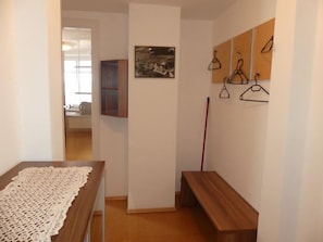 Un couloir avec un banc en bois, un chemin de table en dentelle, un tableau et un porte-manteau avec des cintres.