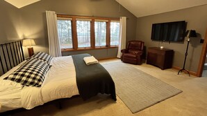 Quarto com cama, cadeira, televisão e janela com cortinas.