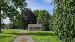 A stone house with a wooden porch, surrounded by lush green grass and trees.