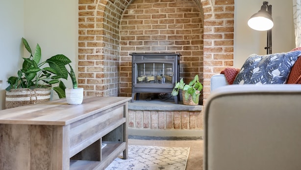 A cozy living room with a brick fireplace, wooden furniture, and potted plants.