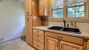A kitchen with wooden cabinets, a granite countertop, a double sink, and a window with a view of trees.