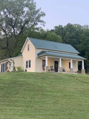 A single-story house with a green metal roof, beige siding, and a front porch with two chairs. - Restored farmhouse just steps from the Katy Trail (Rhineland)