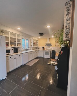 A modern kitchen with white cabinets, a black countertop, and a dark tiled floor. - Restored farmhouse just steps from the Katy Trail (Rhineland)