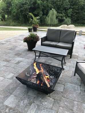 An outdoor patio area with a fire pit table labeled "SECOND CHANCE RIDING," surrounded by a gray sofa, a metal table, and potted plants. - Restored farmhouse just steps from the Katy Trail (Rhineland)