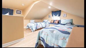 Un dormitorio ático acogedor con dos camas, cada una con colchas a juego, una ventana con cortinas y un escritorio pequeño.