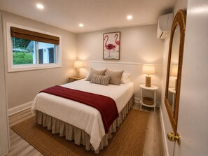 Une chambre à coucher comprenant un lit, deux tables de chevet, une fenêtre, un climatiseur fixé au mur et un miroir.