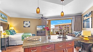 A hotel room with a bed, a dining area, a kitchen, and a balcony with a view of the hotel building. - Maui Resort Rentals: Honua Kai Hokulani 619 - 6th Floor Studio w/ Full Ocean Views! (Lahaina)