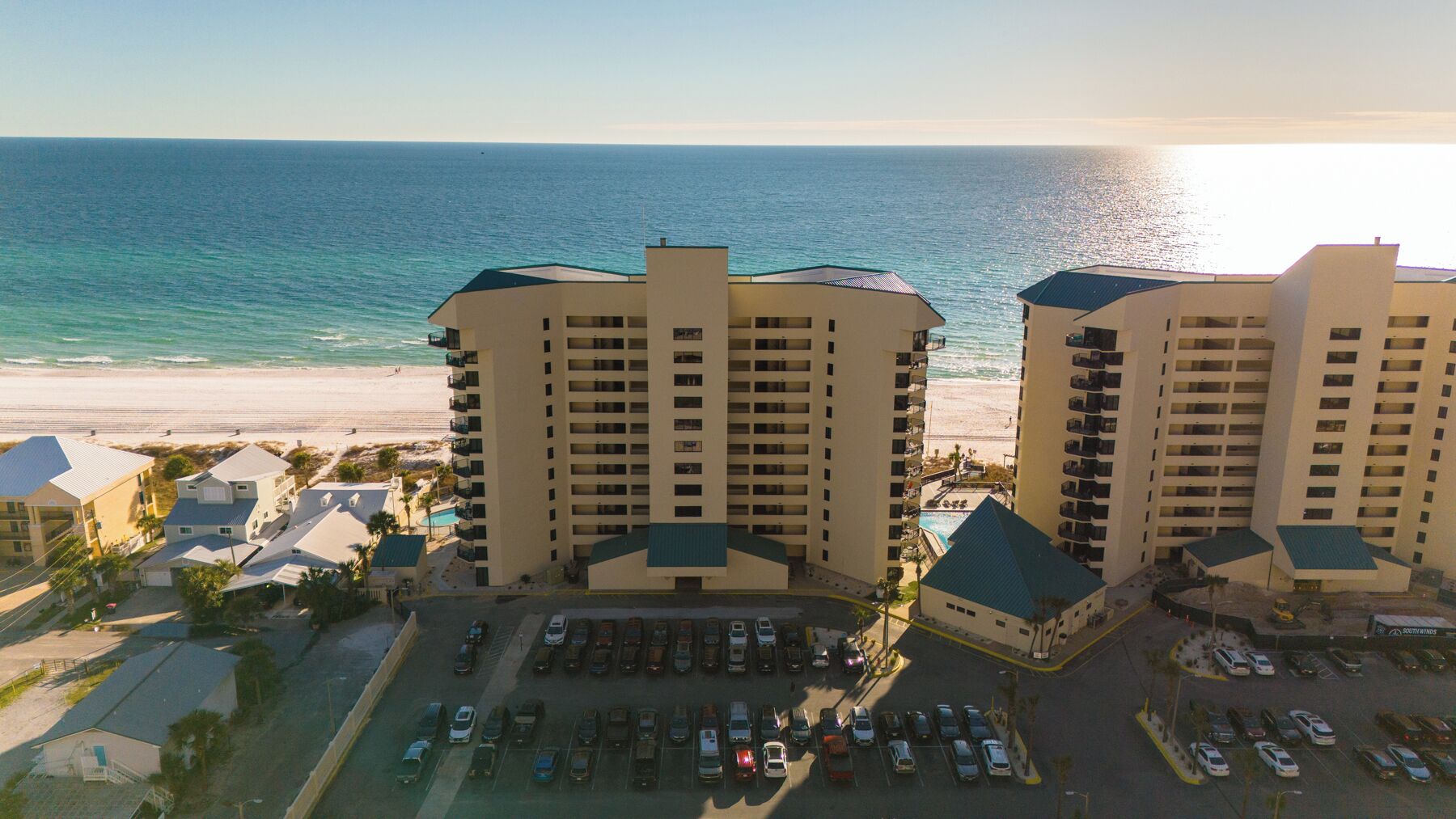 Een strandhotel met meerdere hoge gebouwen, een parkeerplaats en uitzicht op de oceaan.