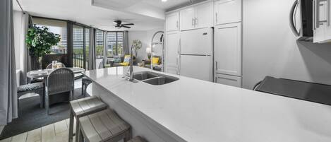 Una cocina moderna con armarios blancos, una isla grande y un comedor con sillas de mimbre.