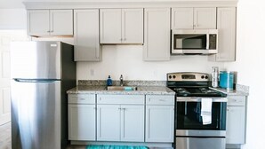 A modern kitchen with stainless steel appliances, light grey cabinets, and a granite countertop. - Surfside 62 - Steps to the Ocean (Crescent City)