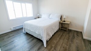 A bedroom with a large bed, a nightstand, a window, and a heater. - Surfside 62 - Steps to the Ocean (Crescent City)