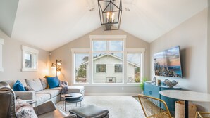 Un salon moderne avec un plafond haut, une grande fenêtre, un téléviseur à écran plat et un coin salon confortable.