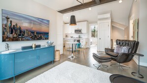 Un salon moderne avec un tableau représentant un paysage urbain, une console bleue, un fauteuil en cuir et un tapis blanc.