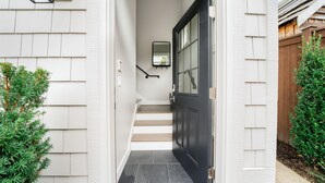 Une entrée de maison avec une porte sombre, un petit escalier et une façade de couleur claire.