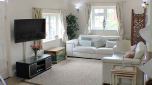 A living room with a white sofa, a flat-screen TV, a small table with a glass, and a potted plant.