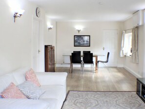 A living room with a white sofa, patterned rug, and a dining area with a table and chairs. - Goudhurst by Interhome (Staplehurst)