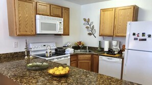 A kitchen with granite countertops, wooden cabinets, a white microwave, stove, and refrigerator. - Walk to Beach! King Size Condo! (Biloxi)