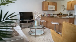 A living room with a sofa, a glass coffee table, a TV, and a plant. - Walk to Beach! King Size Condo! (Biloxi)