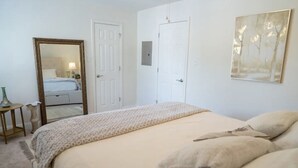 A bedroom with a large bed, two doors, a mirror, and a wall-mounted picture. - Walk to Beach! King Size Condo! (Biloxi)