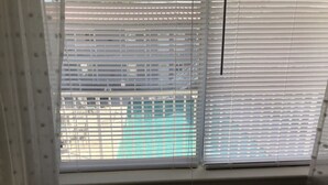 A room with a bed, a window with blinds, and a view of a building outside. - Walk to Beach! King Size Condo! (Biloxi)