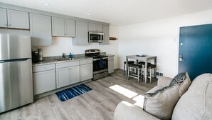 A modern kitchen with grey cabinets, a stainless steel refrigerator, a microwave, and a stove. There is a dining area with a table and chairs. - Steps to the Pacific Ocean!  Fully Remodeled... (Crescent City)