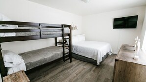 A compact room with a bunk bed, a single bed, a wooden desk, and a flat-screen TV mounted on the wall. - Steps to the Pacific Ocean!  Fully Remodeled... (Crescent City)