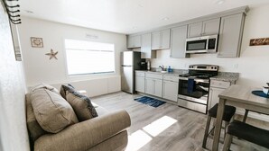 A modern kitchen with grey cabinets, a built-in microwave, a stove, and a refrigerator. There is a window providing natural light and a star decoration on the wall. - Steps to the Pacific Ocean!  Fully Remodeled... (Crescent City)