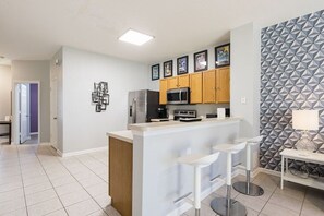 A modern kitchen with a central island, bar stools, a refrigerator, and a microwave. - Featured- 3 Bedroom 3 Bath Private Pool! Windsor Hills (Kissimmee)