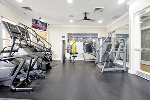 A gym with treadmills, weight machines, and a television screen.