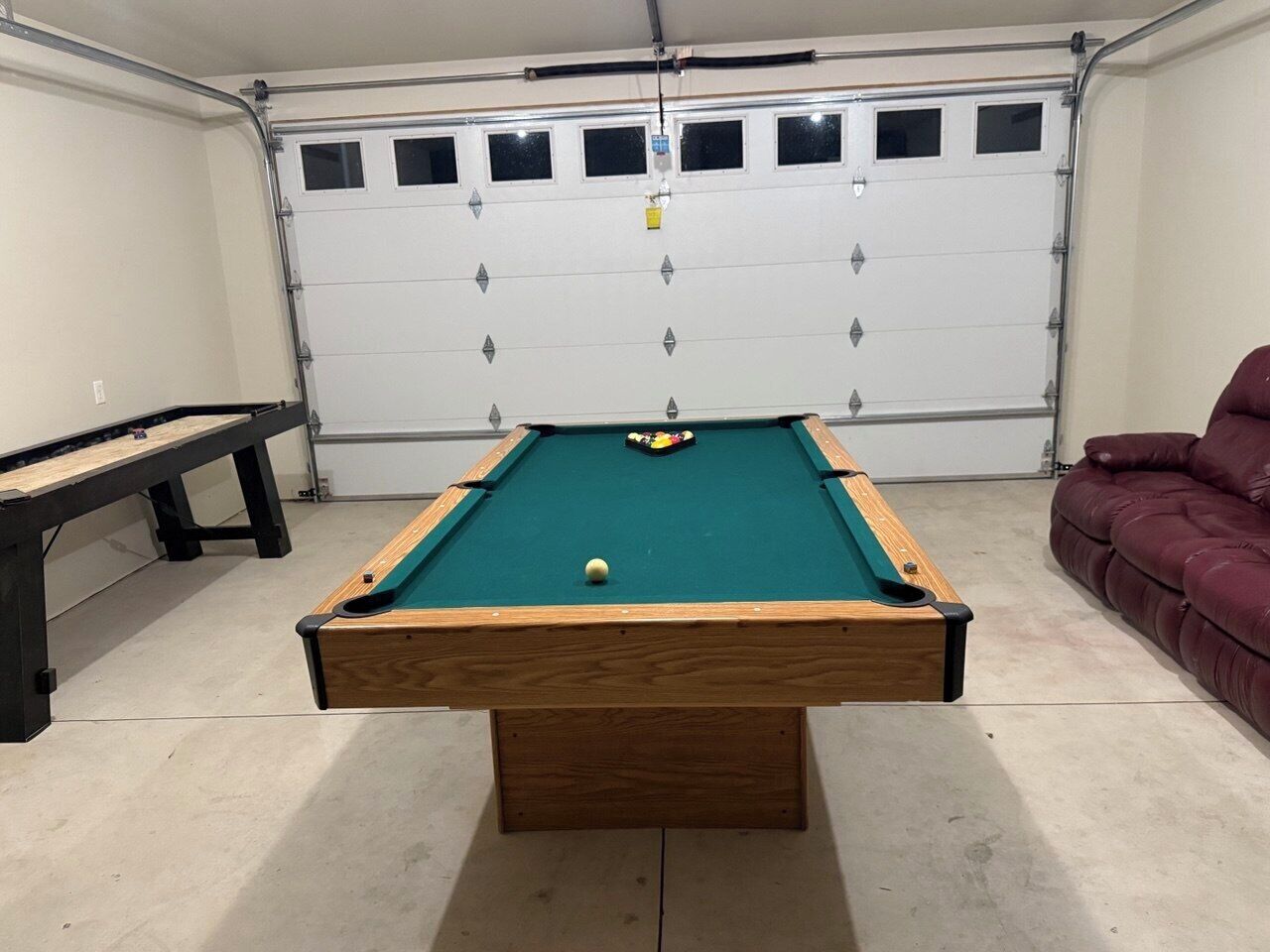 A pool table in a room with a garage door, a bench, and a couch.