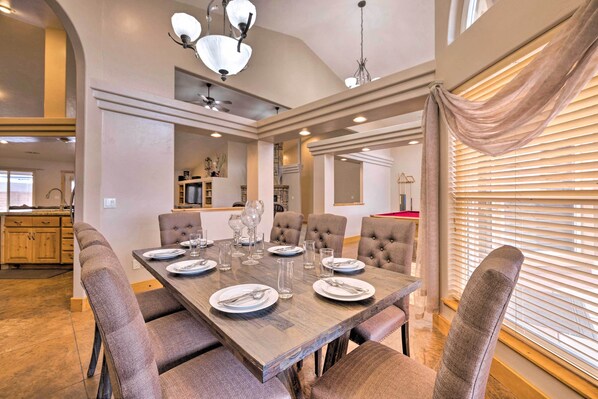 A dining area with a rectangular table set for six, surrounded by upholstered chairs.