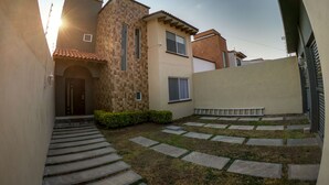 A residential building with a tiled roof, a stone staircase leading to the entrance, and a small garden area with stepping stones. - Beautiful house w heated private pool/ downtown (Tequisquiapan)