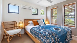 Un dormitorio con cama, una silla, ventilador de techo y ventanas con persianas.