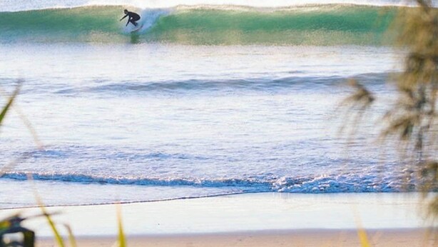 Un surfista montando una ola, con una isla al fondo.