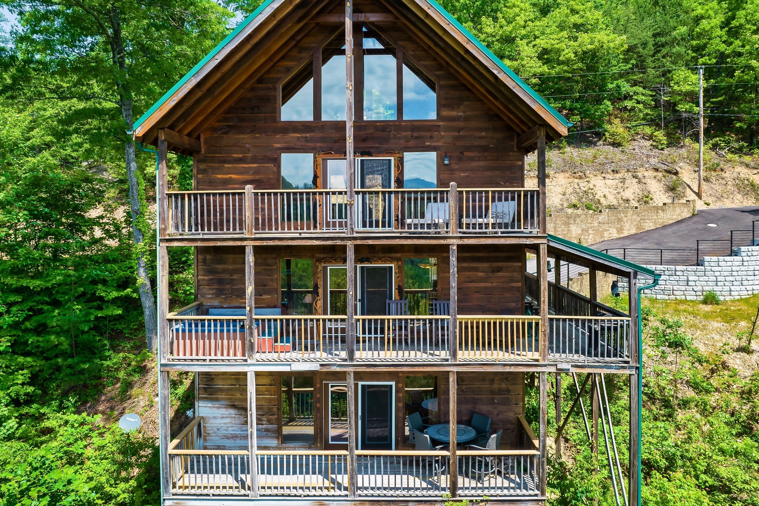 A two-story log cabin with a balcony on each floor, surrounded by lush greenery.