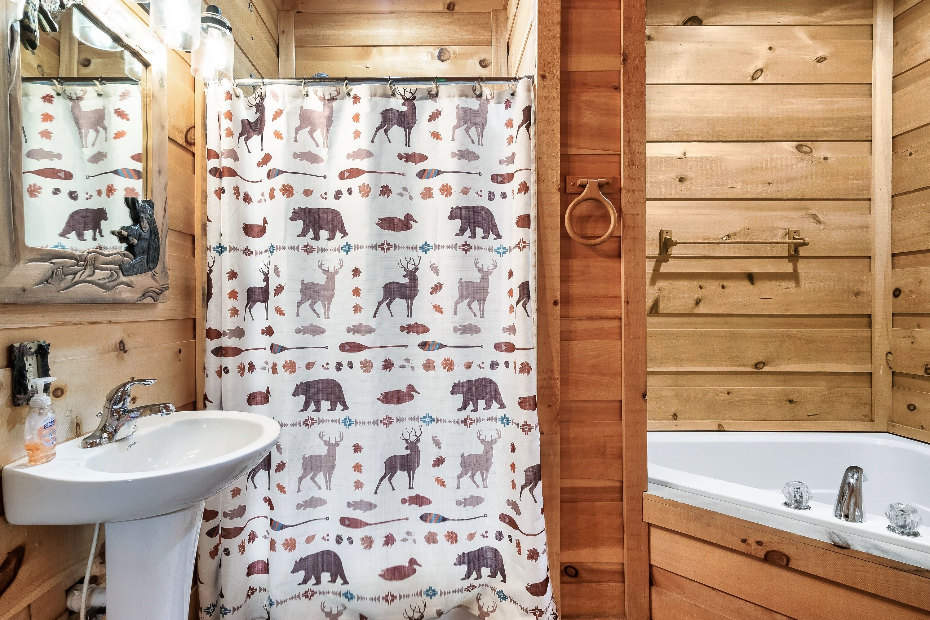 A wooden cabin bathroom with a shower curtain featuring animal prints, a sink, and a bathtub.