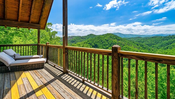 Une terrasse en bois dotée d’un espace salon intégré, offrant une vue sur une forêt verdoyante et luxuriante.