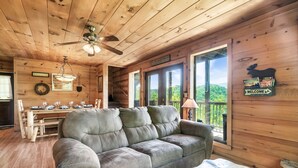 L'intérieur d'un chalet en bois, avec un canapé, une table à manger et de grandes fenêtres.