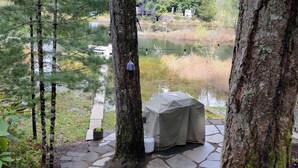 Un chemin de pierre mène à un espace de repos abrité, équipé d’une table et de chaises, et est entouré d’arbres et d’une étendue d’eau.