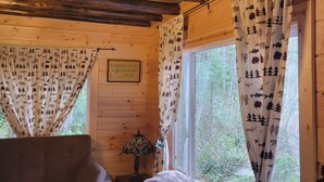 Een knus houten interieur met een bank, een tafel met plaid en gordijnen met een bosmotief.