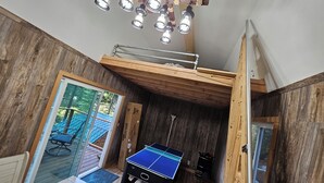 Een kamer met een tafeltennistafel, houten wanden en een plafond met hangende lampen.
