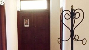 A hallway with a wooden floor, a dark door with a small picture, and a black metal stand with a curved design.