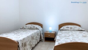 A bedroom with two single beds, each with a wooden headboard and a patterned bedspread. There is a bedside table with a lamp between the beds.